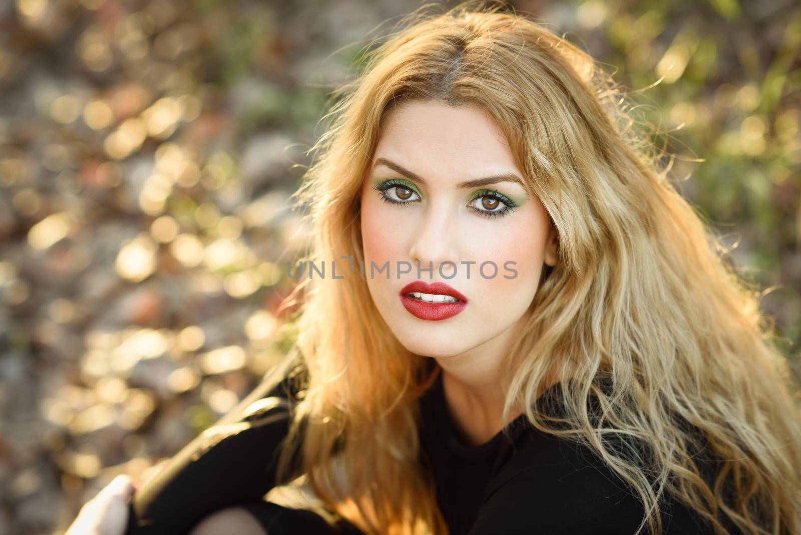 Close-up portrait of blong woman in rural background. Relaxed girl lying on the field with long curly hair.