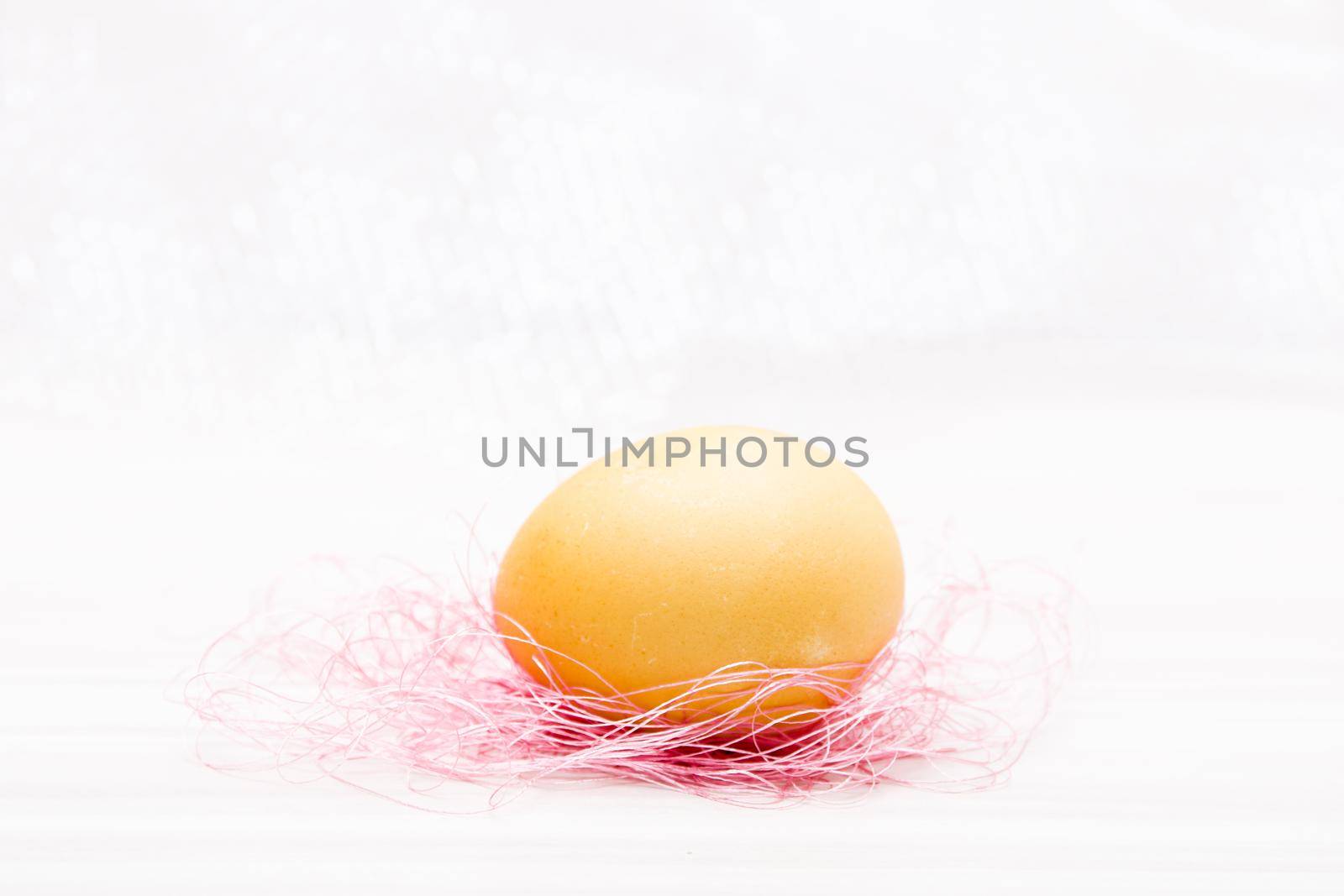 yellow easter egg on pink threads copy space white background