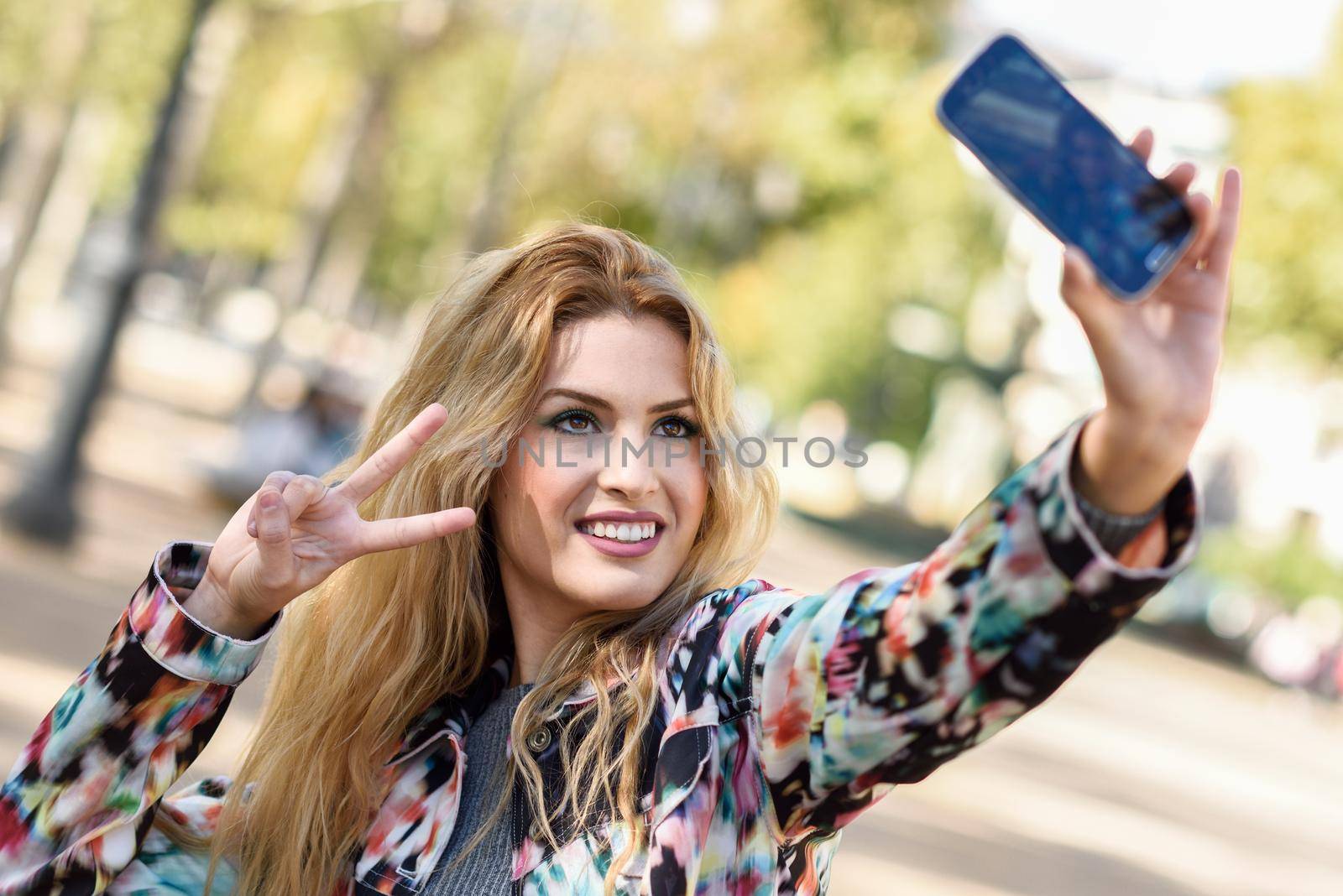 Portrait of a beautiful young woman selfie in the park with a smartphone