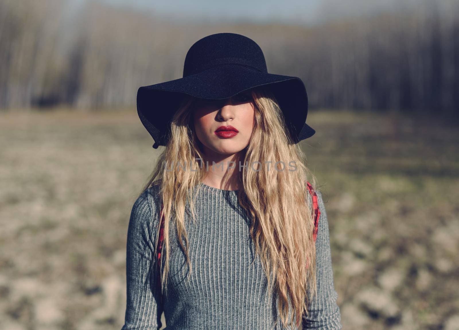 Beautiful young blonde woman, model of fashion, in rural background. Girl wearing sweater, skirt and hat.