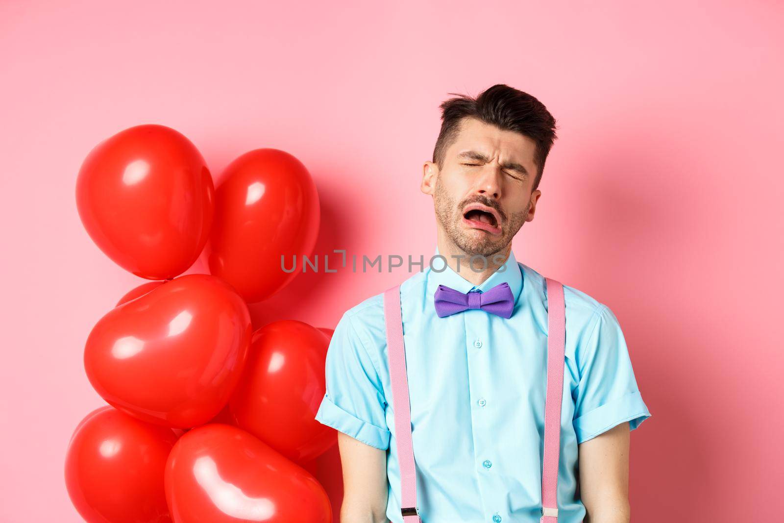 Valentines concept. Sad and heartbroken man crying over break-up, being cheated on lovers day, sobbing and feeling lonely, standing on pink background.