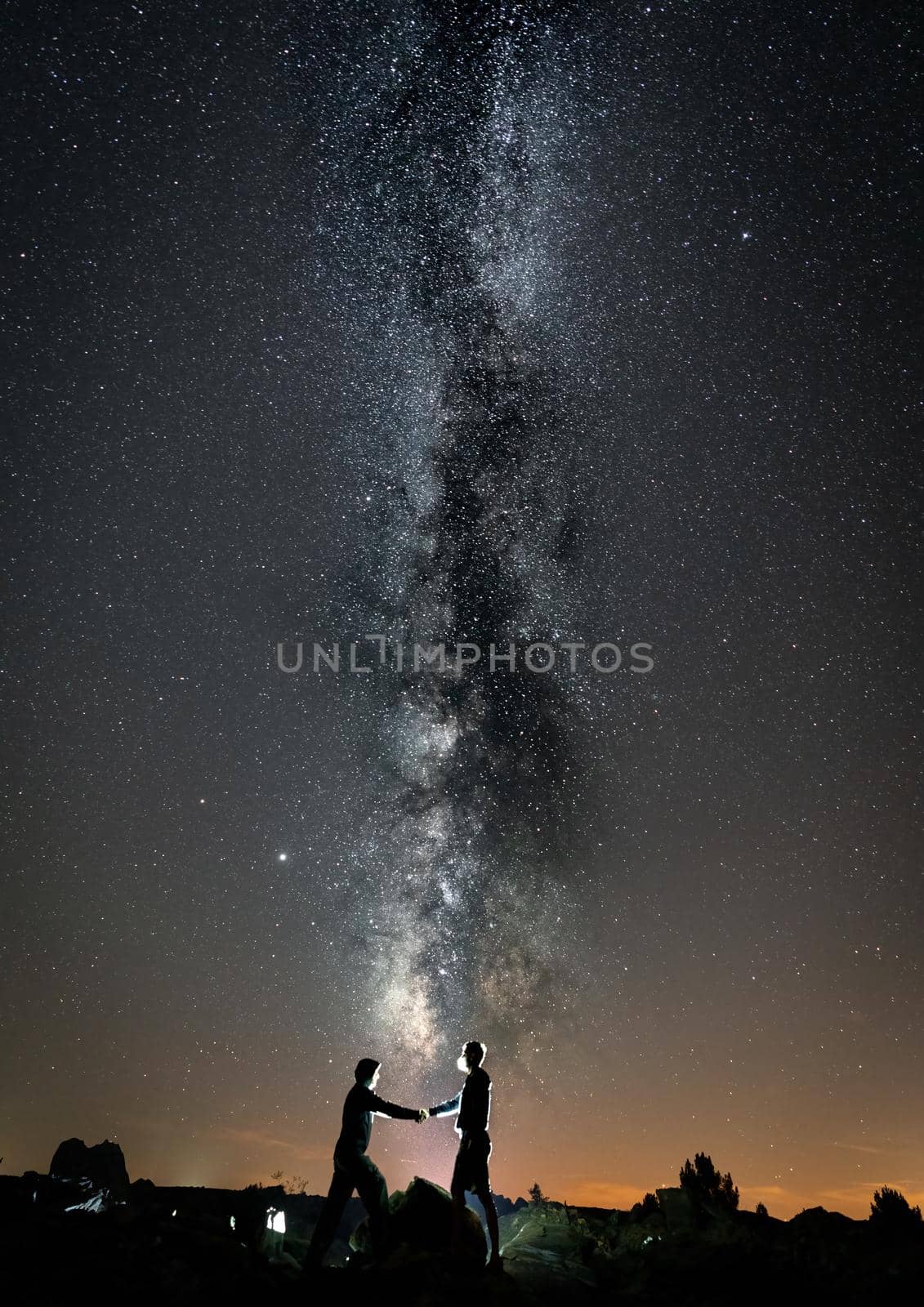 Two persons with masks shaking hands against milky way, vertical composition