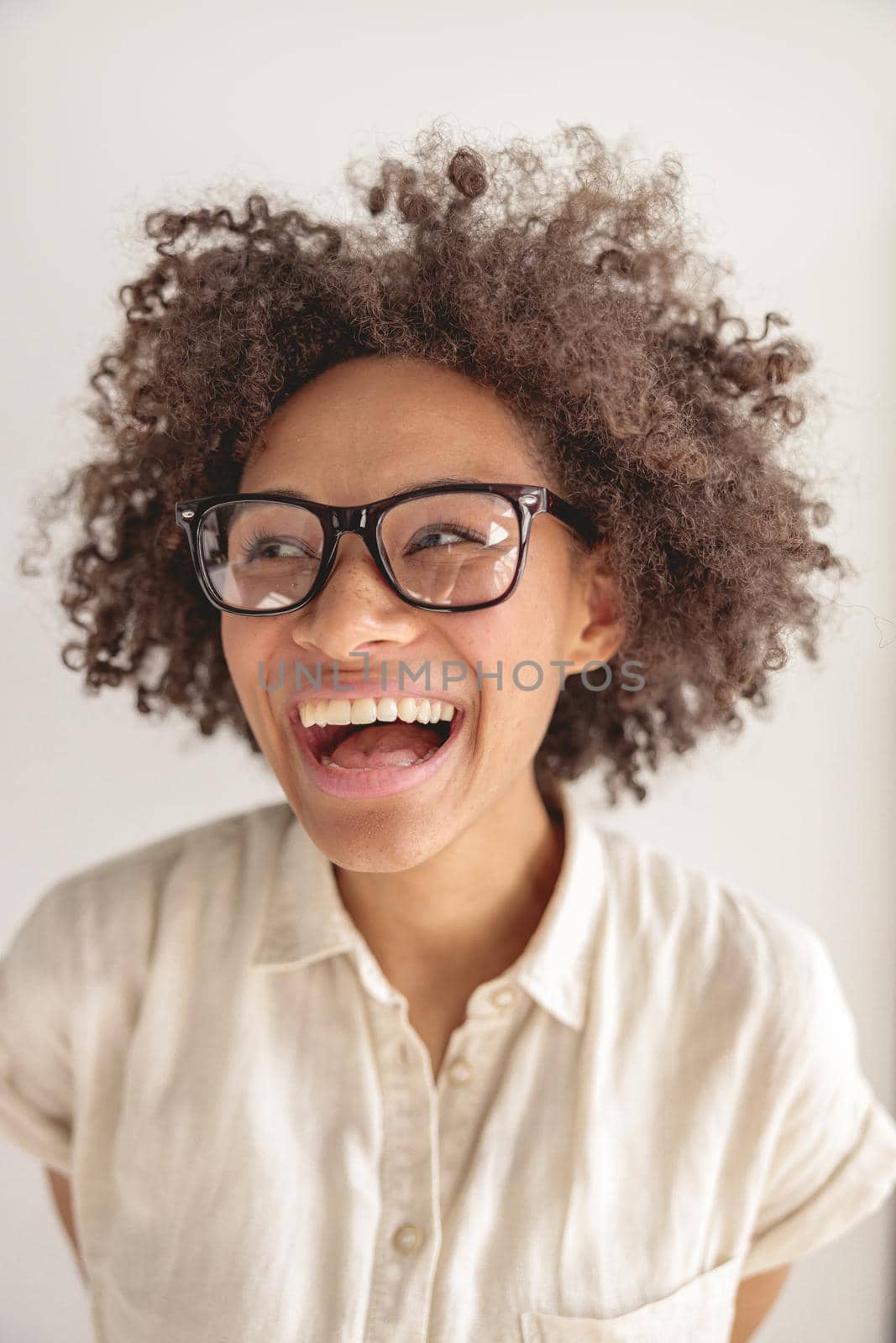 Portrait of young Afro American lady in glasses laughing and looking away, isolated on grey background