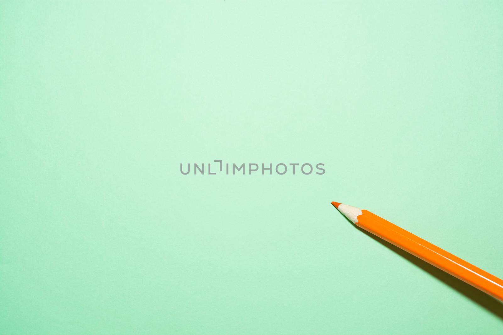 One orange pencil on a light green background with a dark shadow.