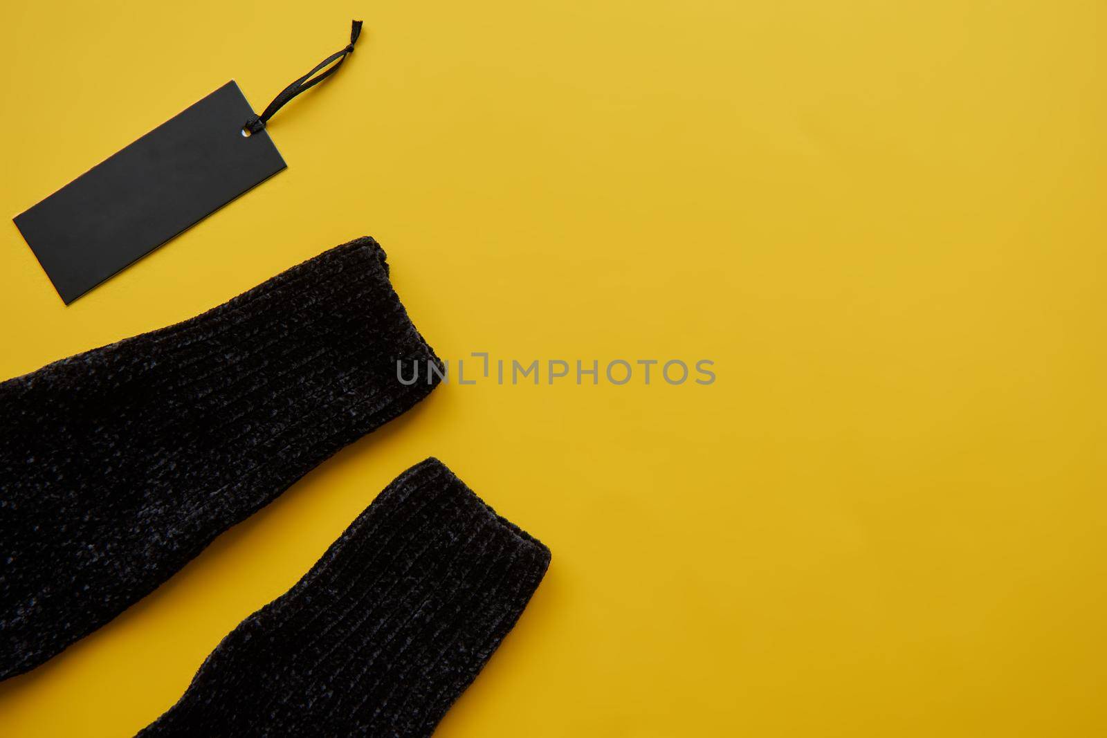 Black cosy pullover and paper label isolated on yellow paper background. Clothing tag, label blank mockup template, to place your design. Black friday final sale banner by OneWellStyudio