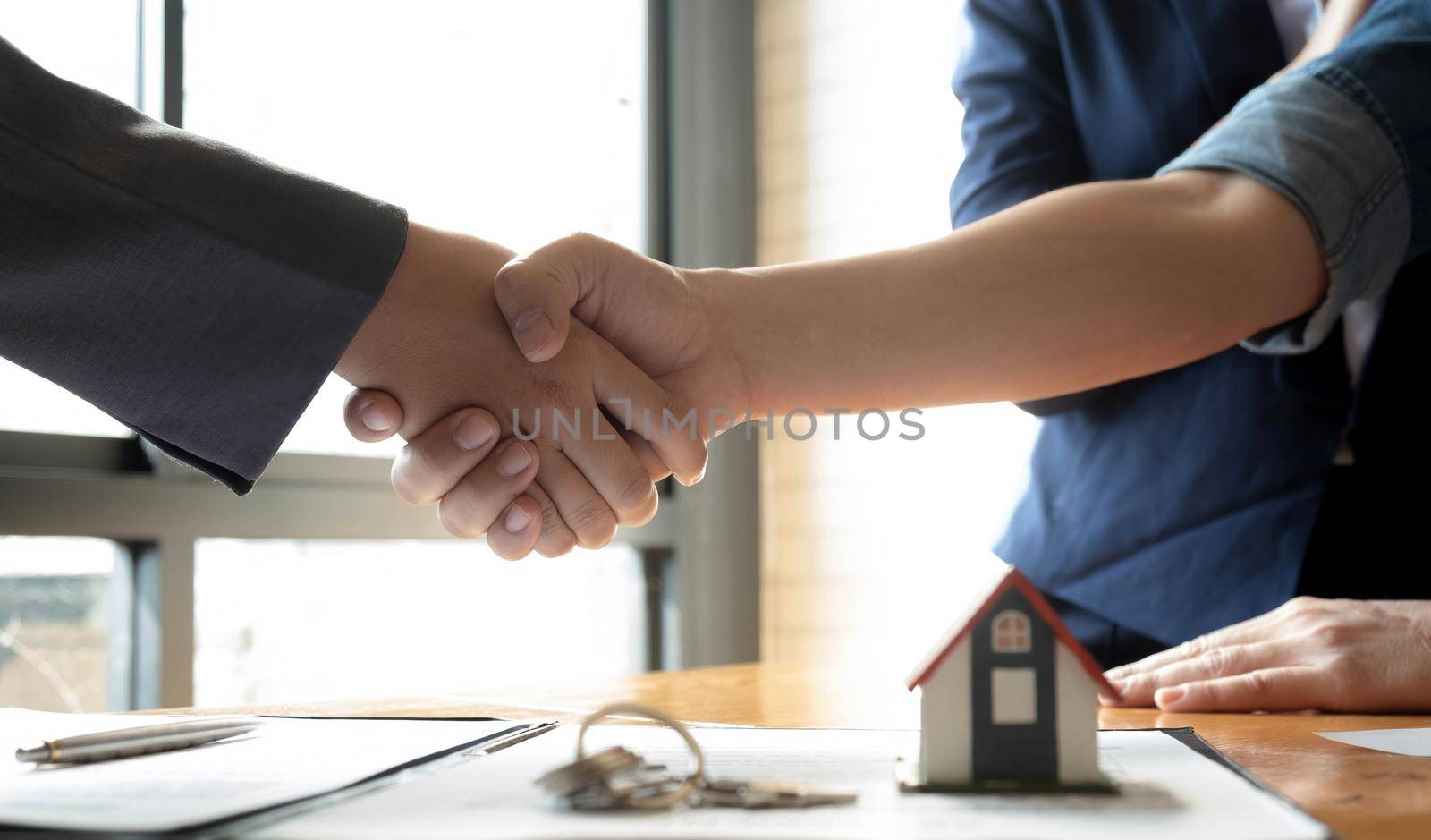 Real estate broker and customer shaking hands after signing a contract: real estate, home loan and insurance concept by wichayada