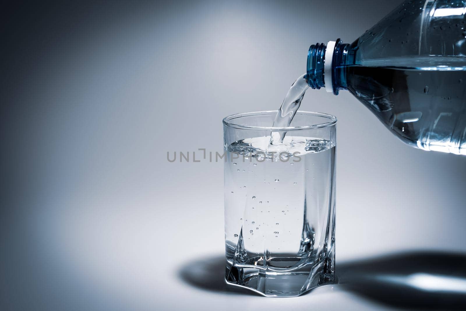 Pouring water into a glass from a plastic bottle. Light contrasting background with veneering.