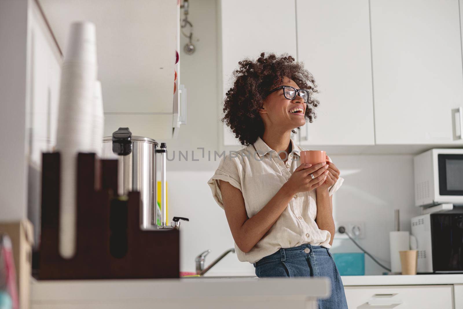 Pretty Afro American woman in glasses standing in modern office kitchen interior