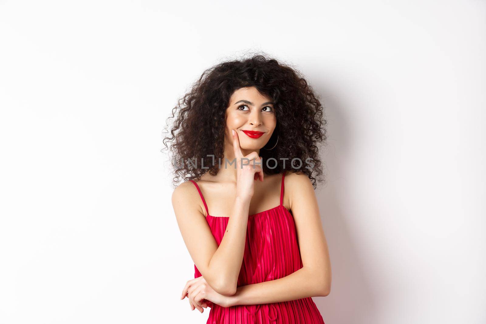 Image of elegant woman in red dress, looking pensive and smiling, thinking of romantic date, standing over white background by Benzoix
