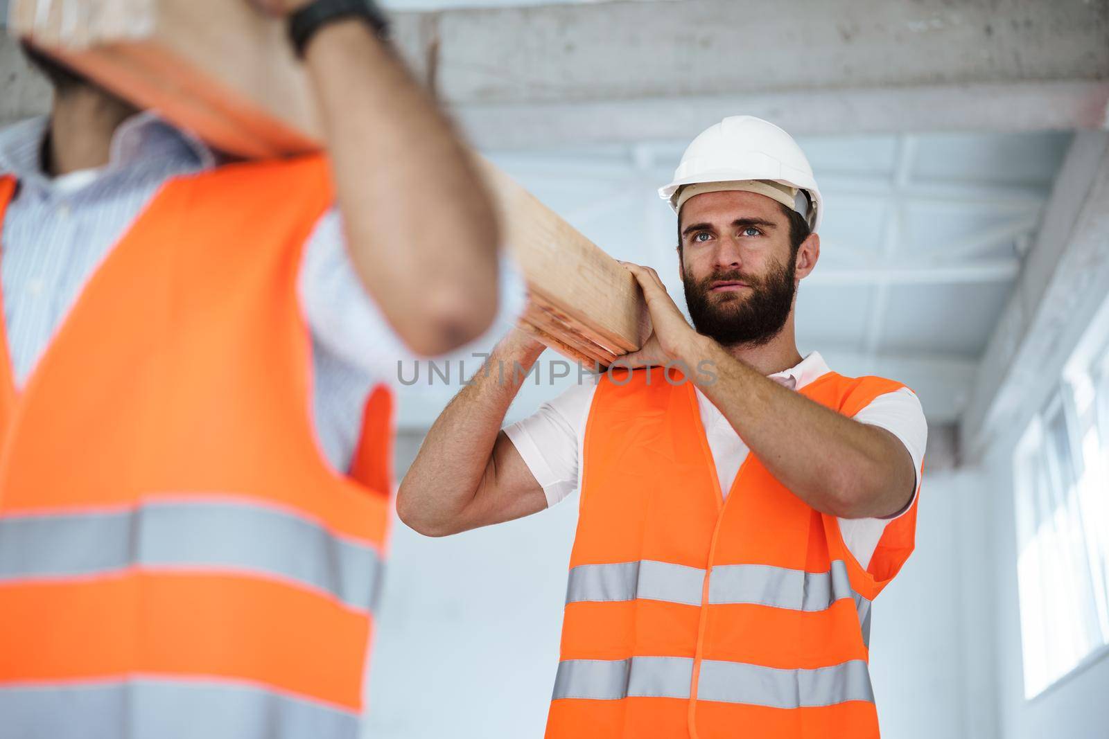 Two young men builders carrying wood planks on construction site, close up photo