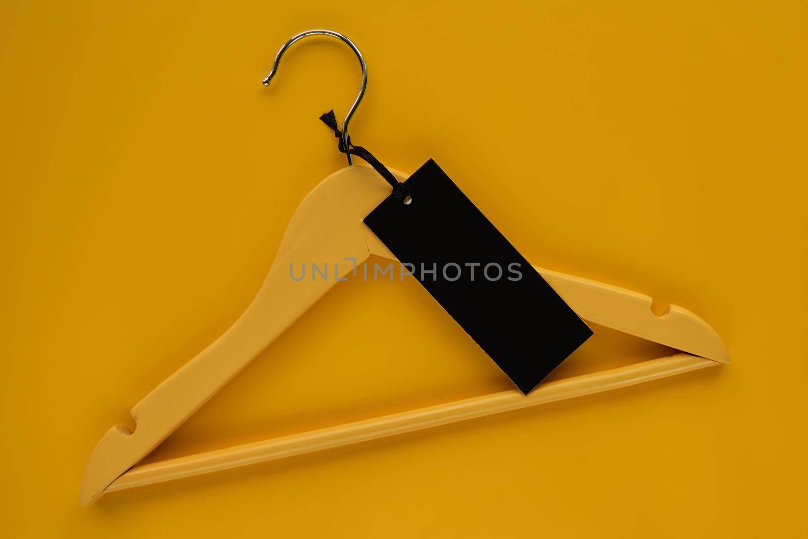 Wooden Coat hanger with black paper label isolated on yellow paper background. Clothing tag, label blank mockup template, to place your design. Black friday final sale banner by OneWellStyudio