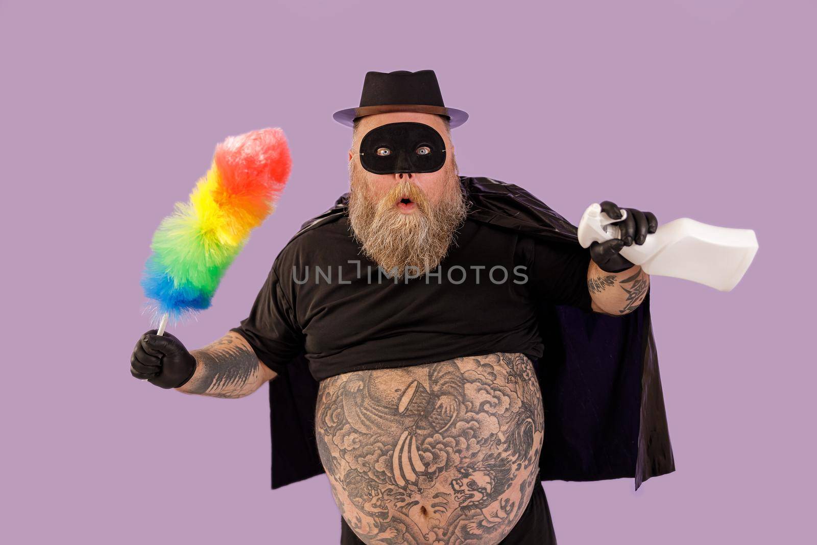 Surprised man with overweight in carnival suit holds brush and spray bottle on purple background by Yaroslav_astakhov