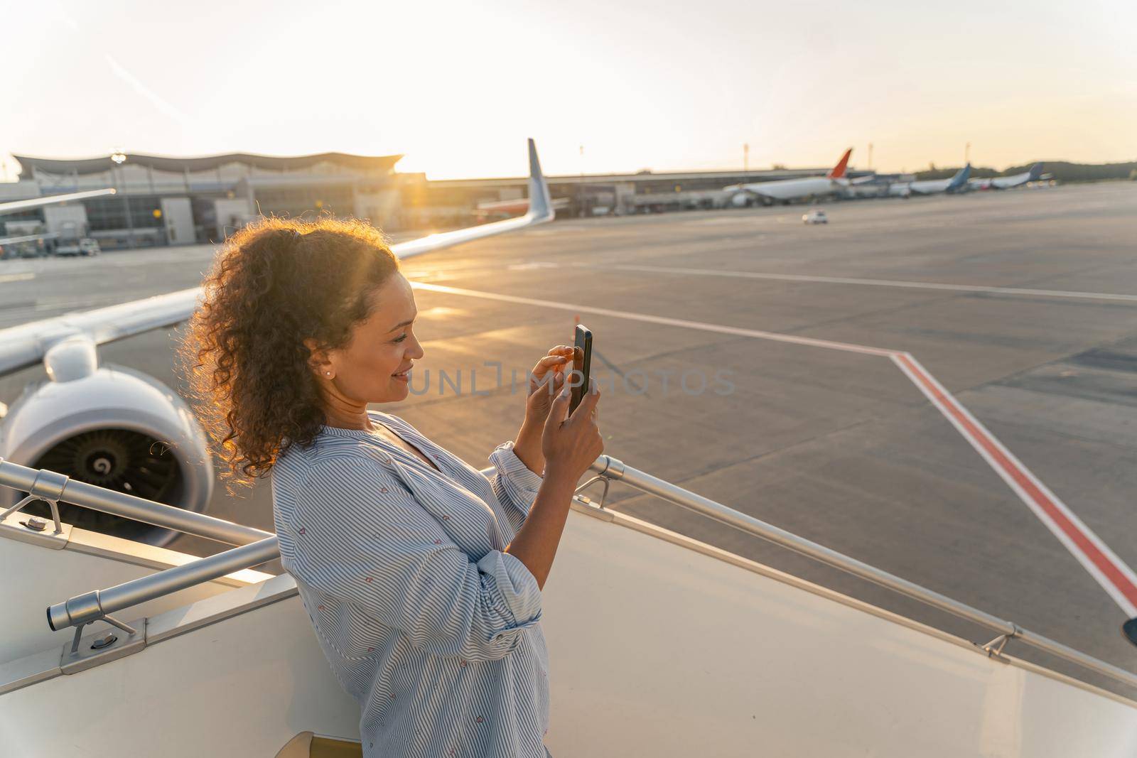 Relaxed lady using smartphone while standing on the plane ladder and taking a photo. Travel concept