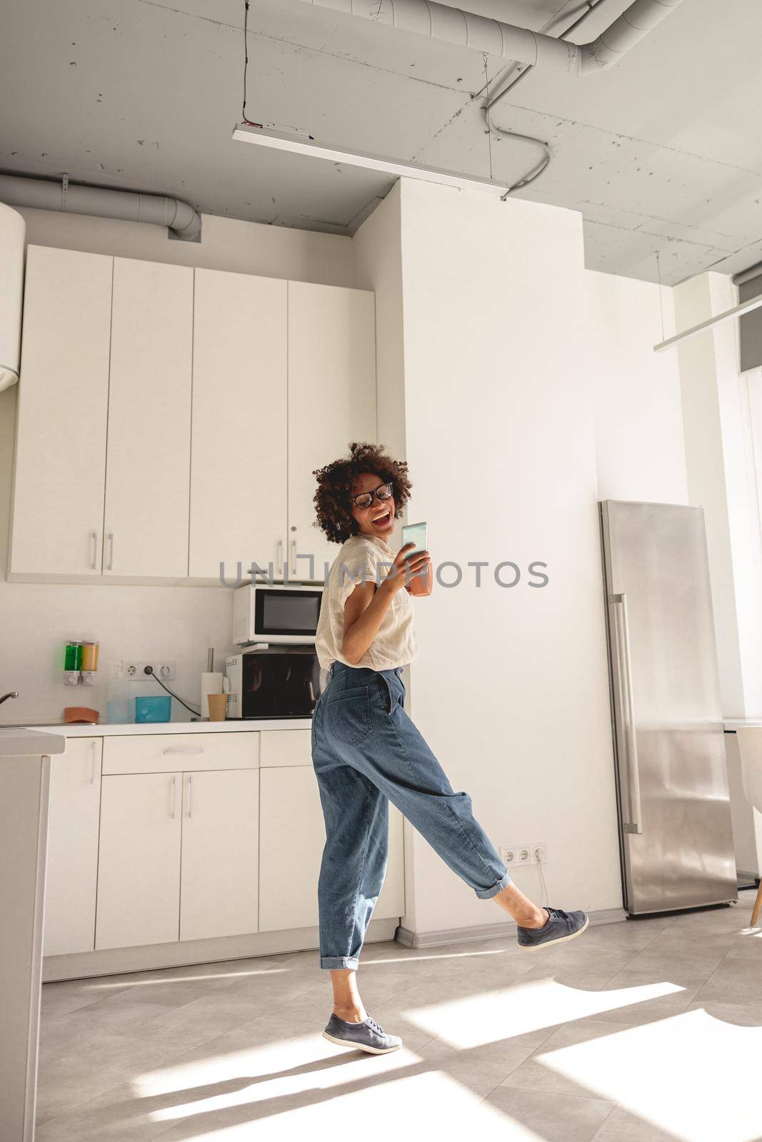 Positive Afro American woman in glasses listening to music and dancing by Yaroslav_astakhov