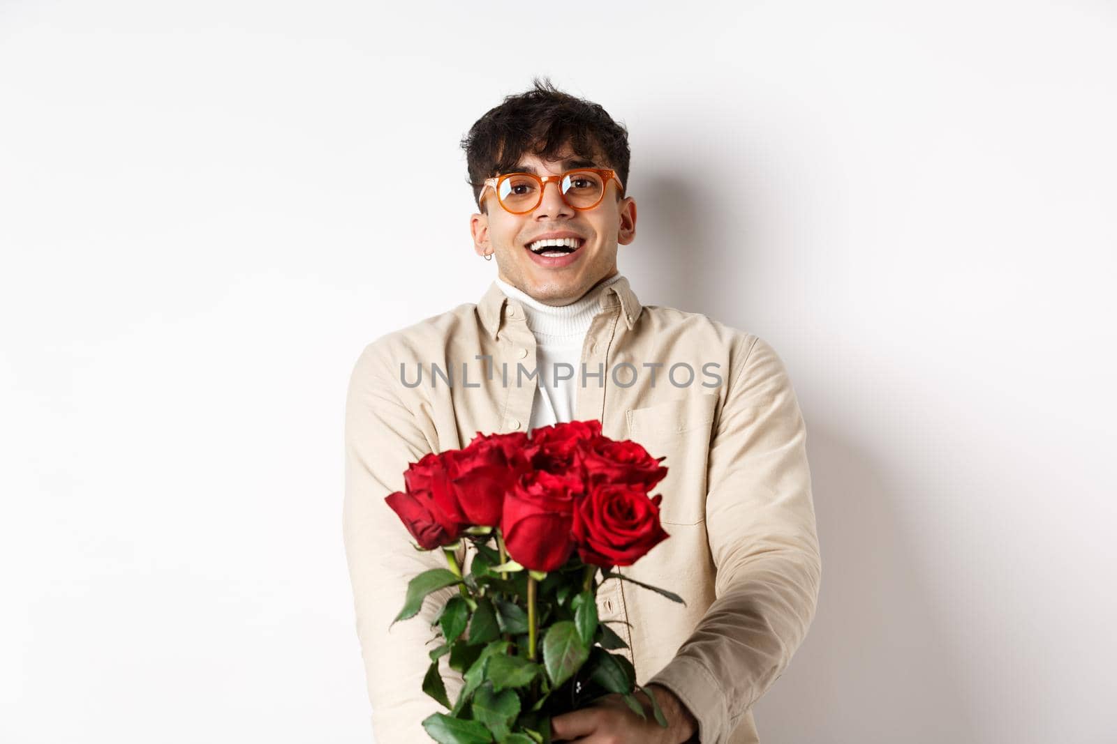 Man in love holding red roses and looking tenderly at camera, staring at lover with happy face, celebrating Valentines day with girlfriend, standing over white background by Benzoix