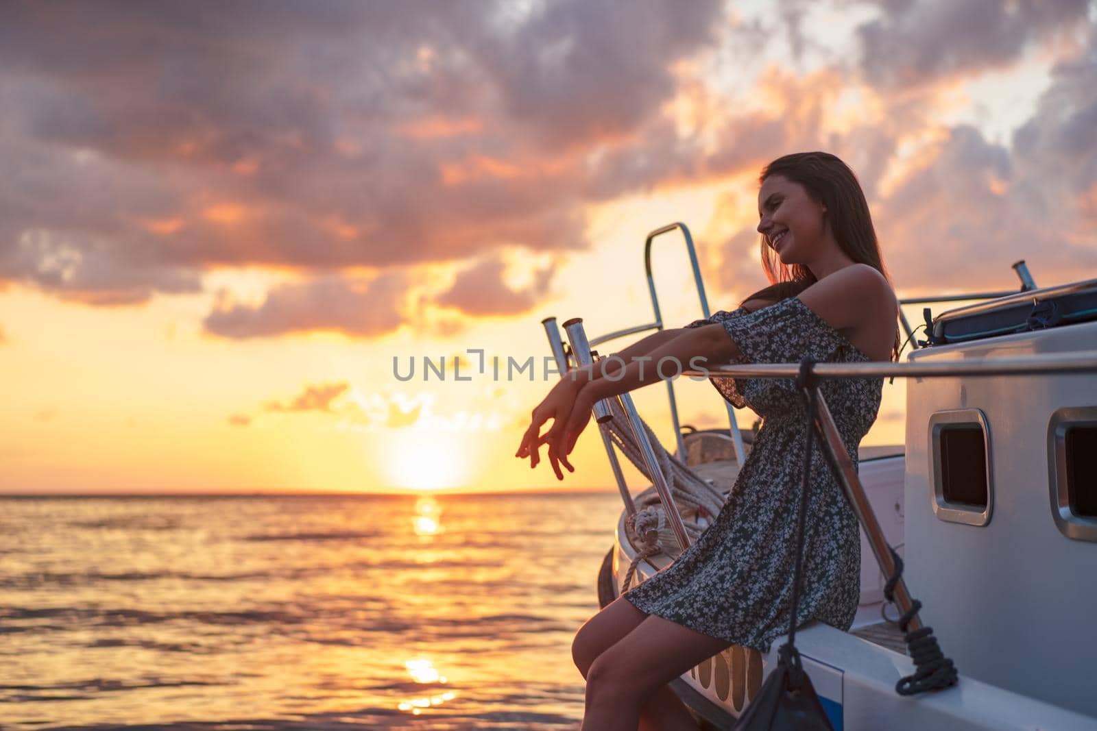 Young attractive woman sitting on the deck of the yacht and enjoying sunset