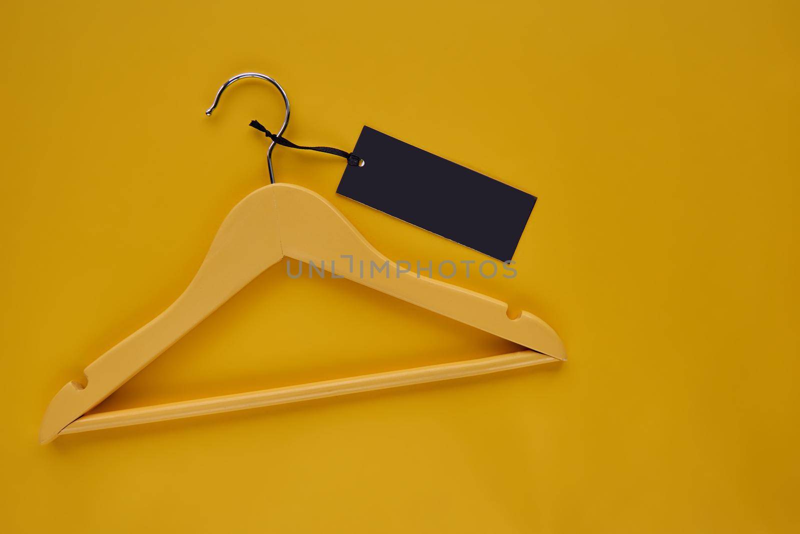 Wooden Coat hanger with black paper label isolated on yellow paper background. Clothing tag, label blank mockup template, to place your design. Black friday final sale banner.