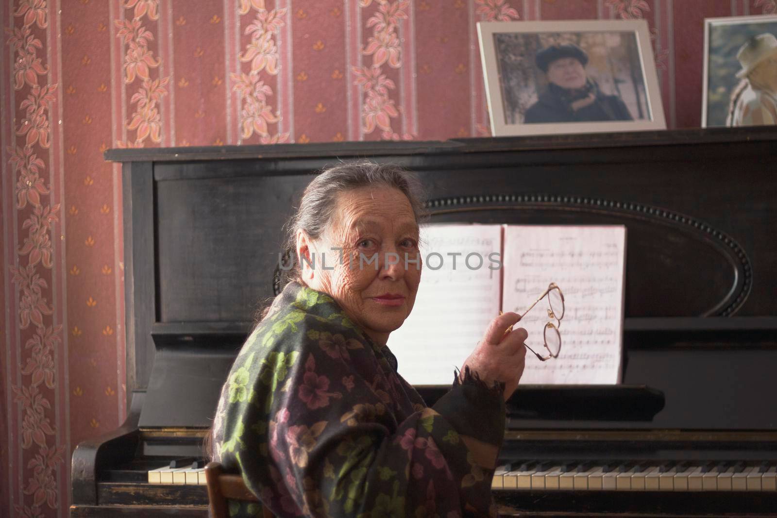 The old lady sitting in front of a piano with her glasses in her hands, active ageing