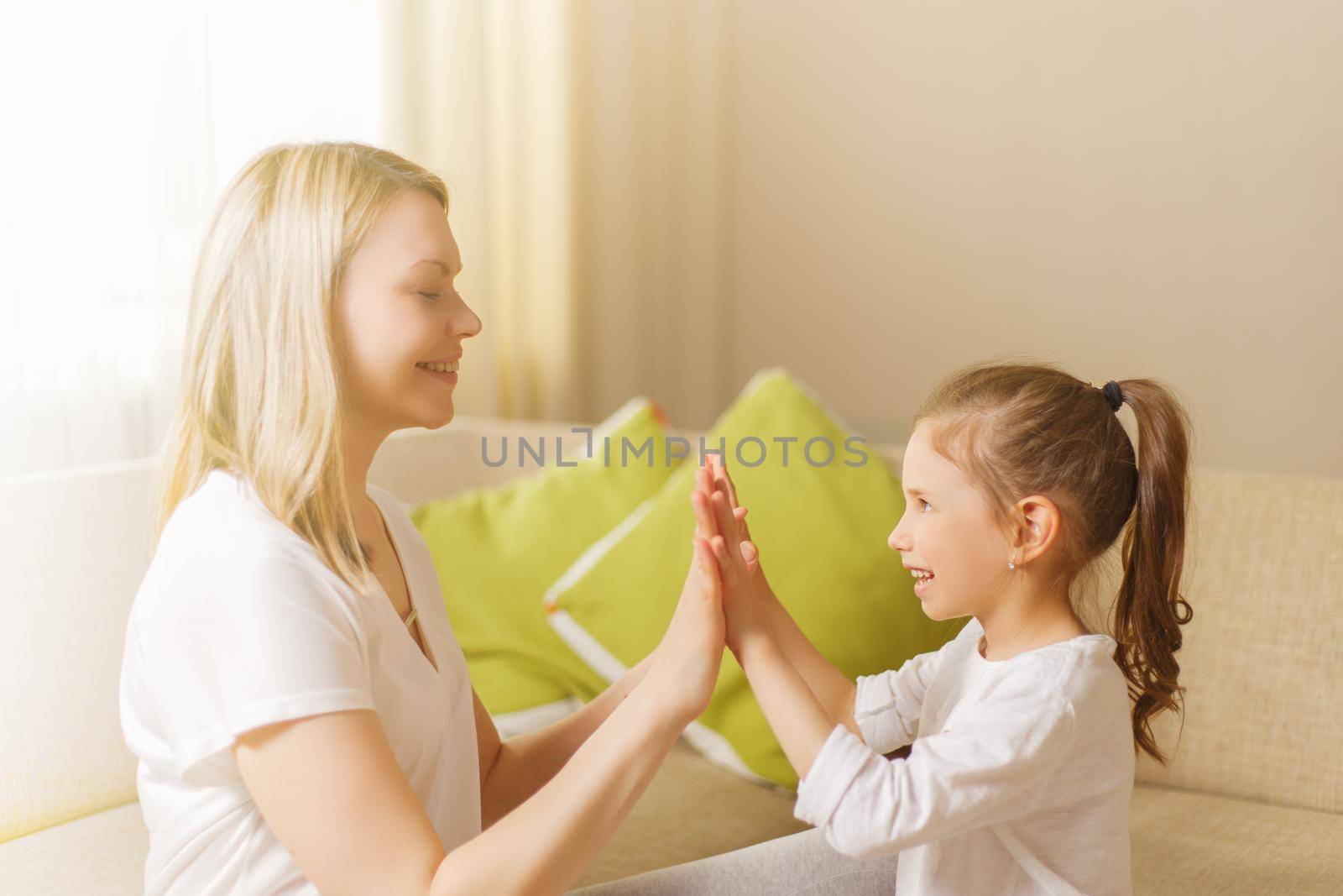 Cute little girl and her beautiful mother are playing games at home, clapping hands together. by alf061