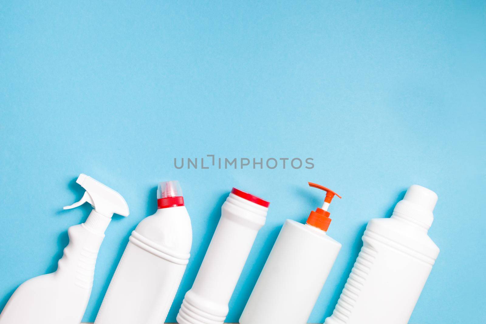 various types of white plastic bottles without labels for detergents on a light blue background; top view copy space, detergent powder bottle, toilet cleaner, liquid soap and spray bottle