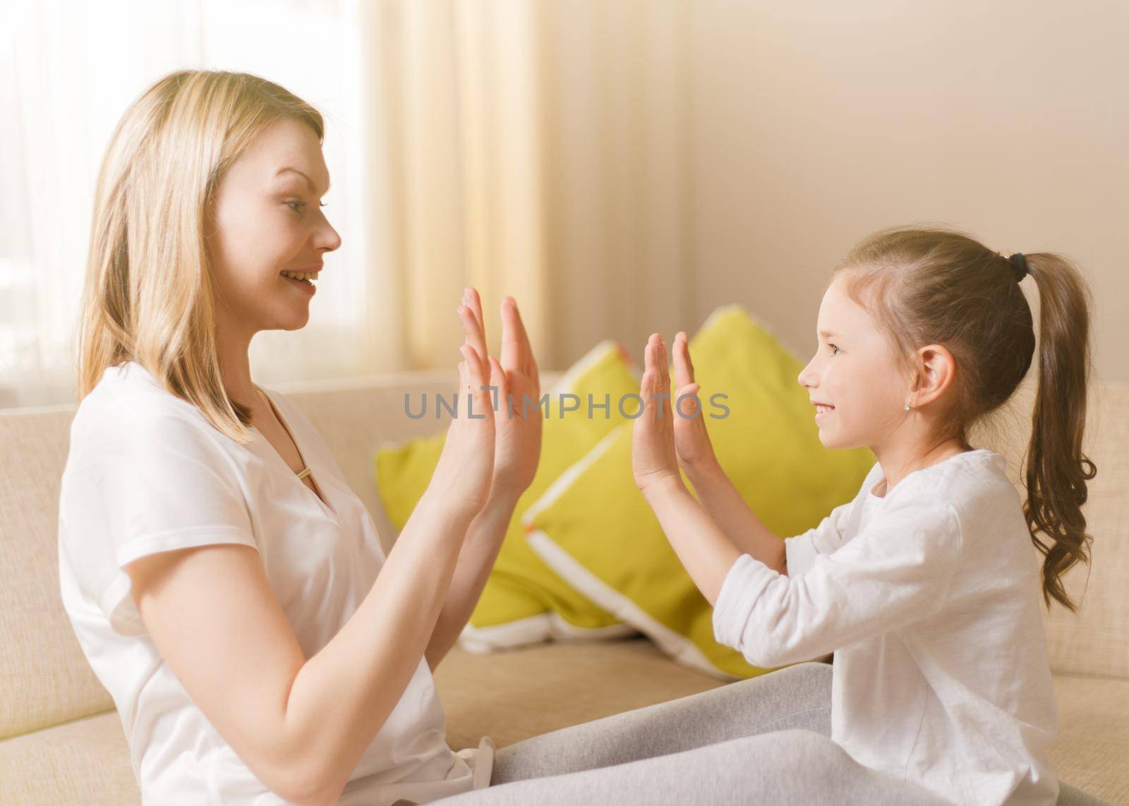 Cute little girl and her beautiful mother are playing games at home, clapping hands together.