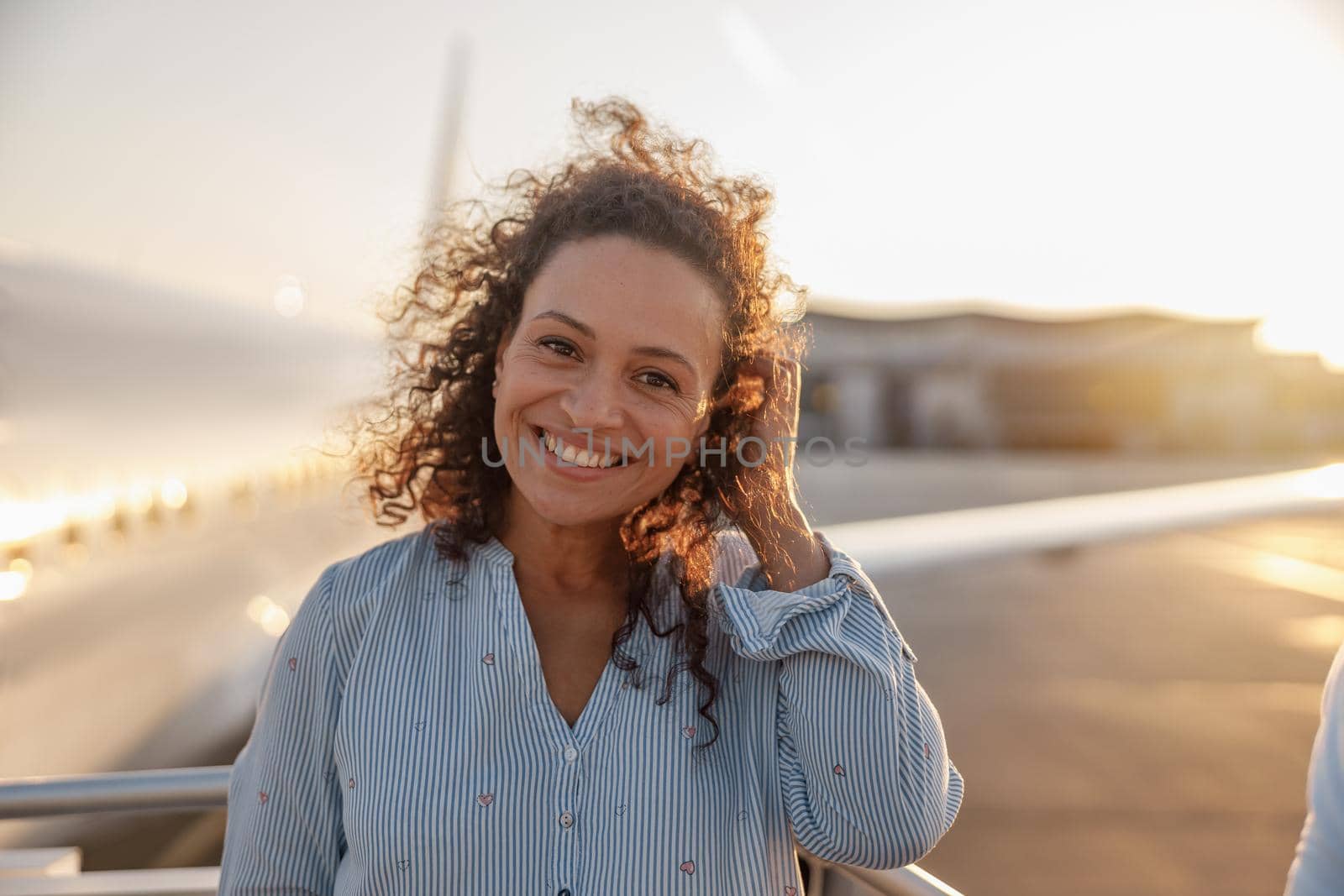 Portrait of happy female tourist, cheerful woman smiling at camera while standing outdoors ready for boarding the plane at sunset by Yaroslav_astakhov