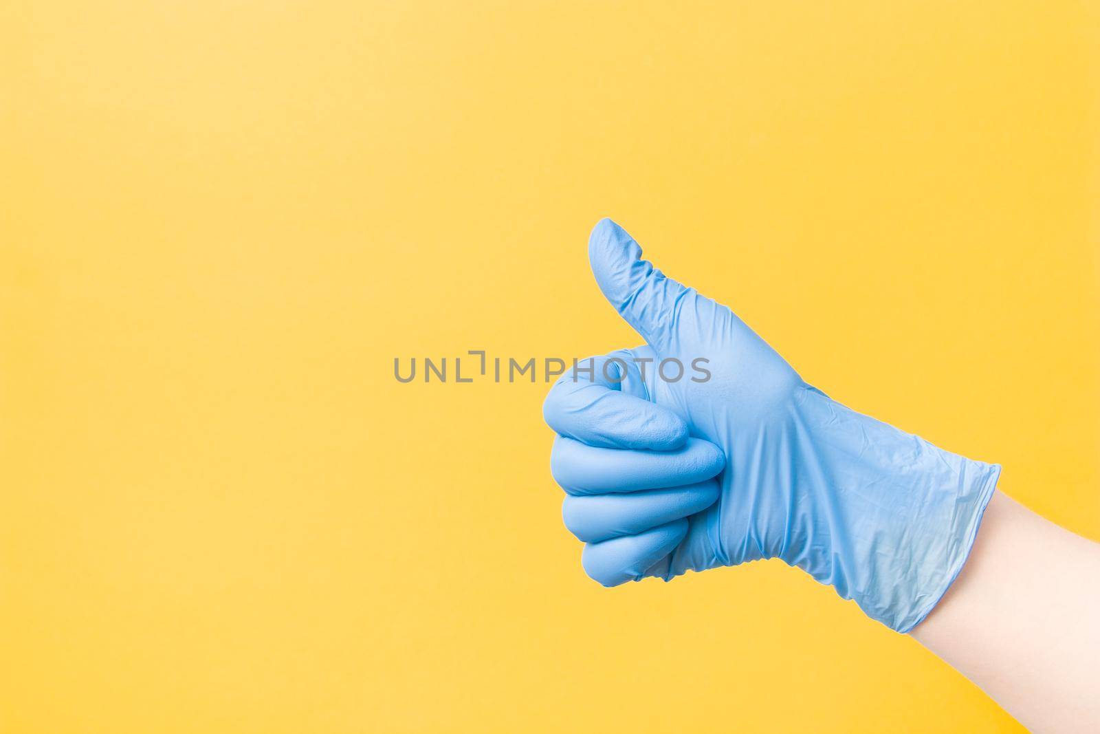 hand in a blue disposable medical glove with a raised thumb up on a yellow background copy space, ok sign, approval gesture and like sign concept