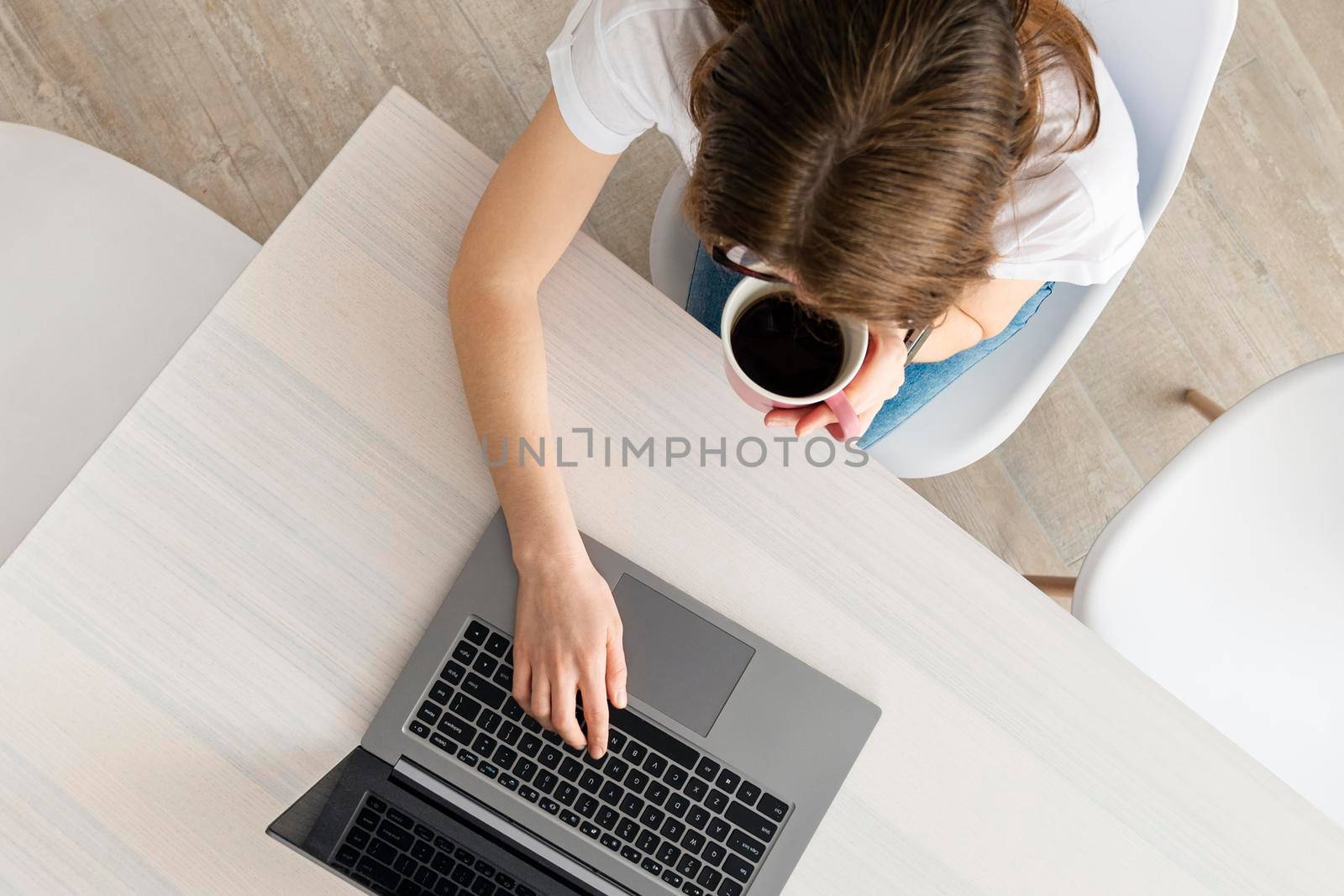 Top view on young Woman working on the laptop in modern place. Home office concept. Girl, laptop, table with coffee cup in modern coworking