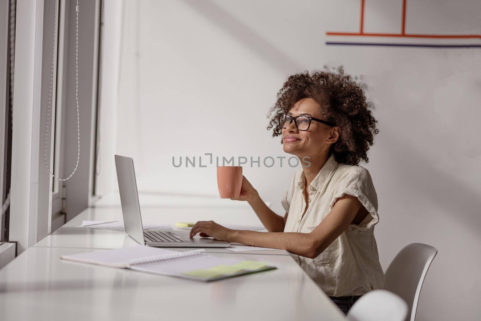 Smiling woman working with laptop and holdng coffee in hand by Yaroslav_astakhov