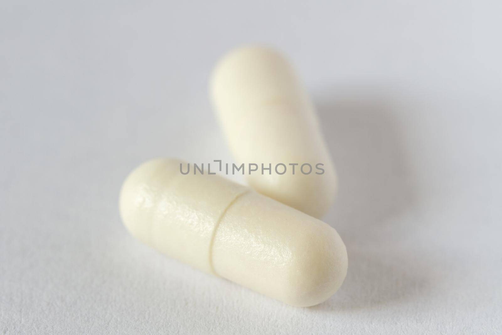 Two white pills capsule on light background. Macro, selective focus