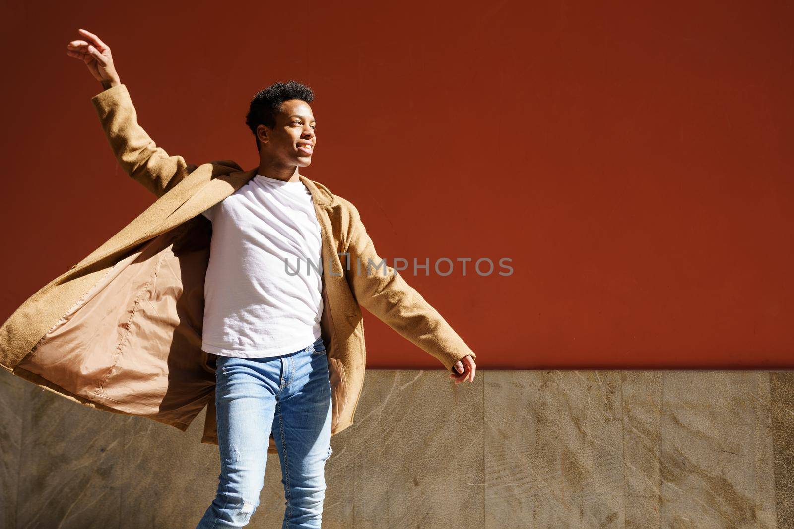 Young black man dancing on red urban wall. Happy Cuban guy outdoors.