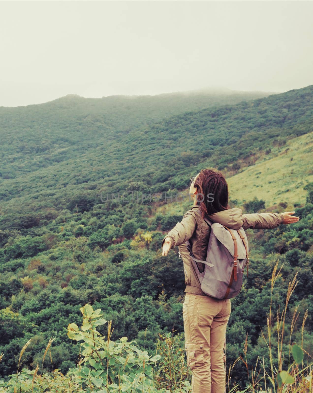 Happy traveler explorer young woman with backpack standing with raised arms and enjoying a beautiful nature.