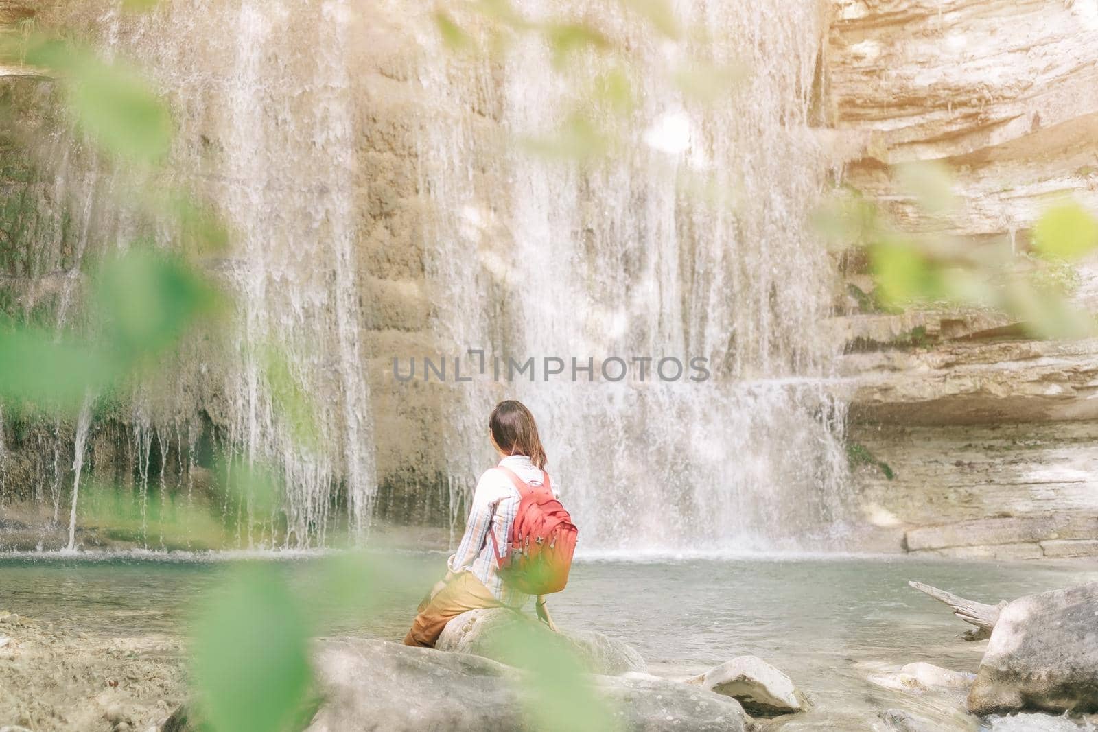 Backpacker young woman resting in front of waterfall in summer outdoor.