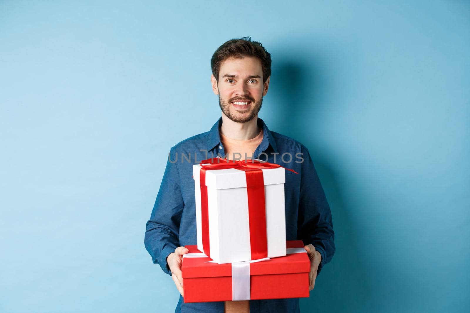Happy valentines day. Handsome boyfriend holding gifts for lover on romantic date anniversary, standing over blue background.