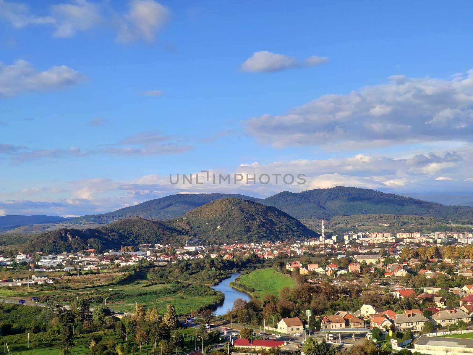 Small european city with small river on low mountains background at bright autumn day