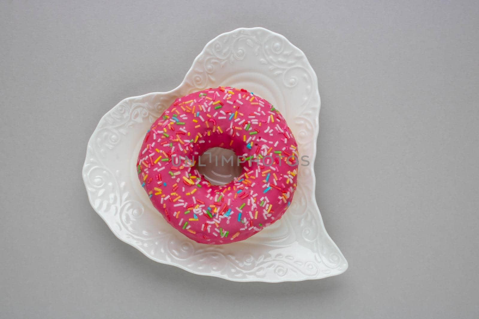 Donut with colorful sprinkles isolated lying on a white plate on gray background. Top view by lapushka62