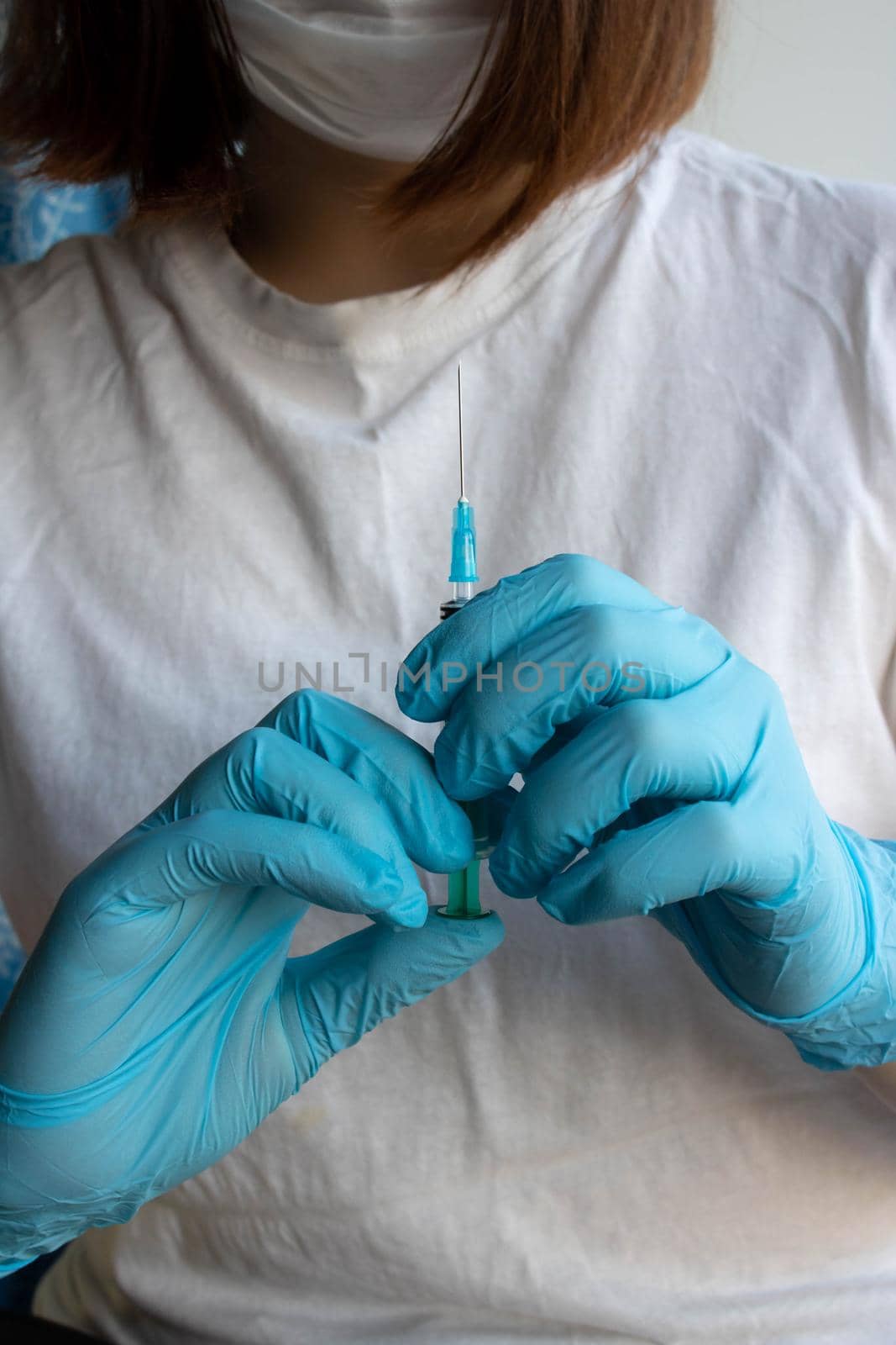 A syringe with a needle in the hand of a girl in a surgical mask and medical gloves.