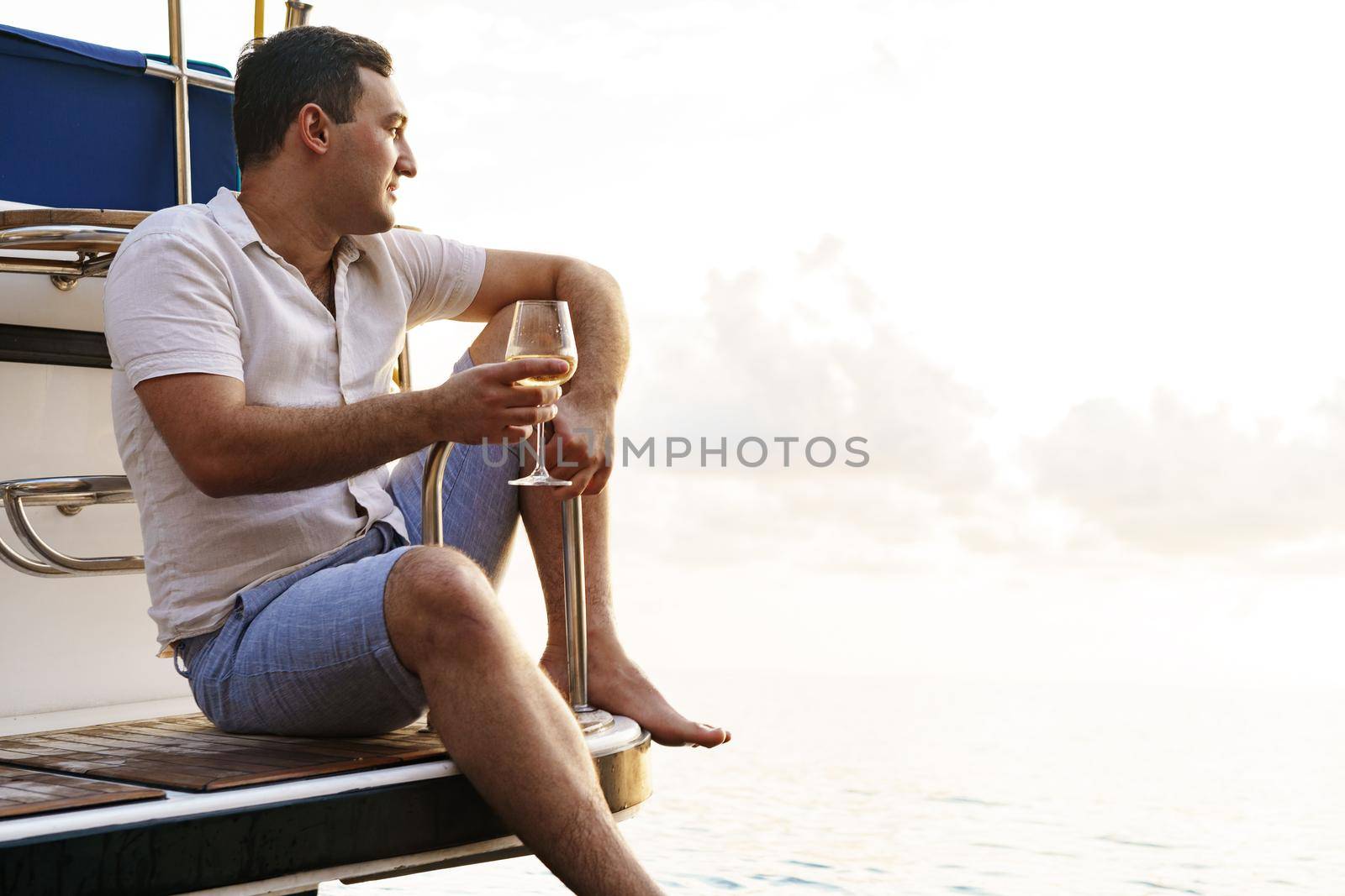 Young man holding a glass of wine on an open deck of a cruise boat, close up