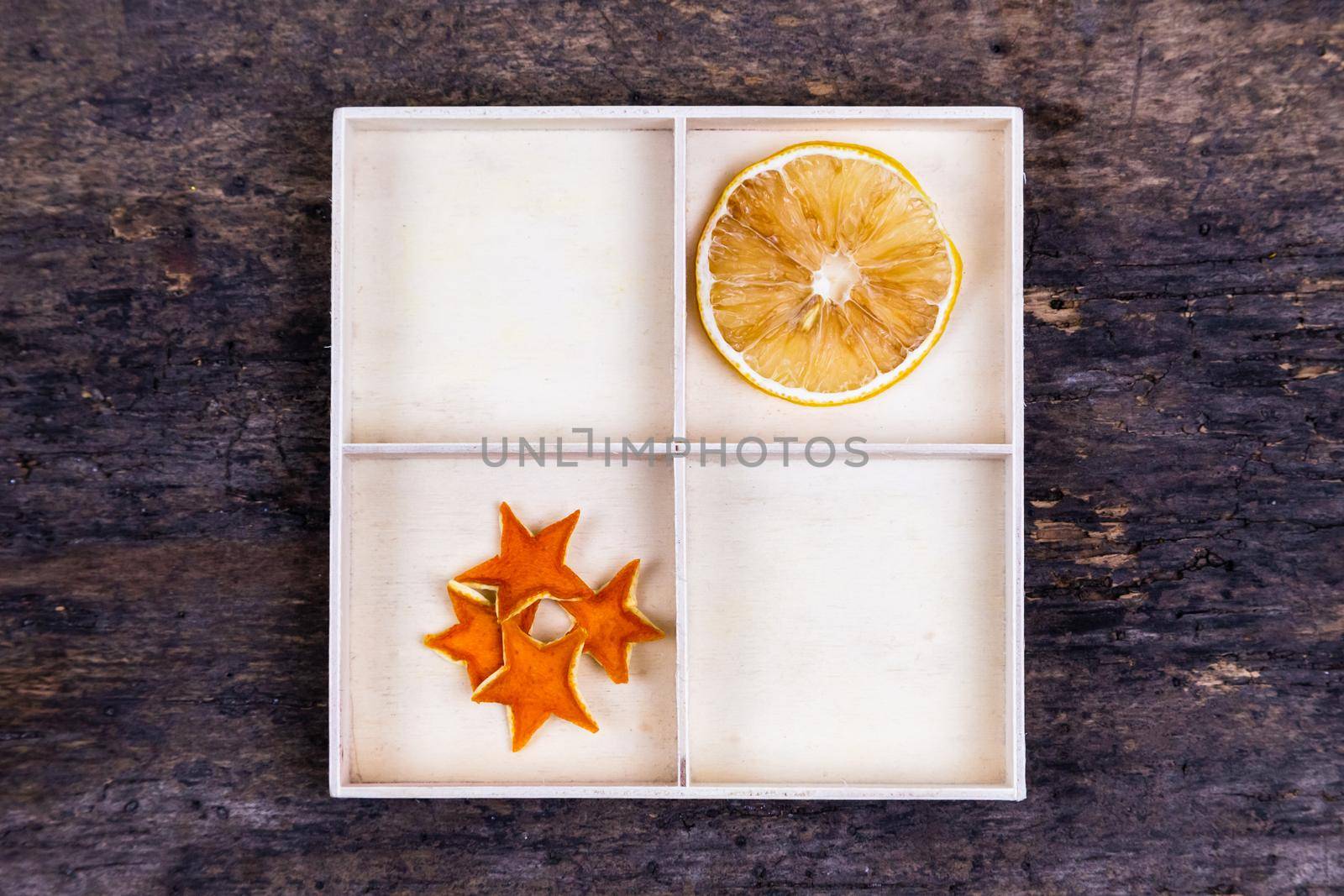 A white box with compartments on a wooden background filled with dried oranges and tangerine stars by lunarts