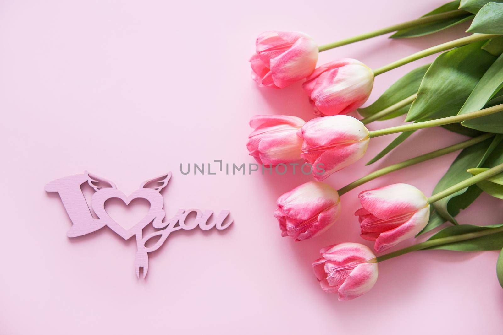 Pink Tulip flowers, a tree cutting are placed on a pink background. The view from the top, smooth lay. The concept of spring. Women's day. Valentine's day. Wooden inscription I love you