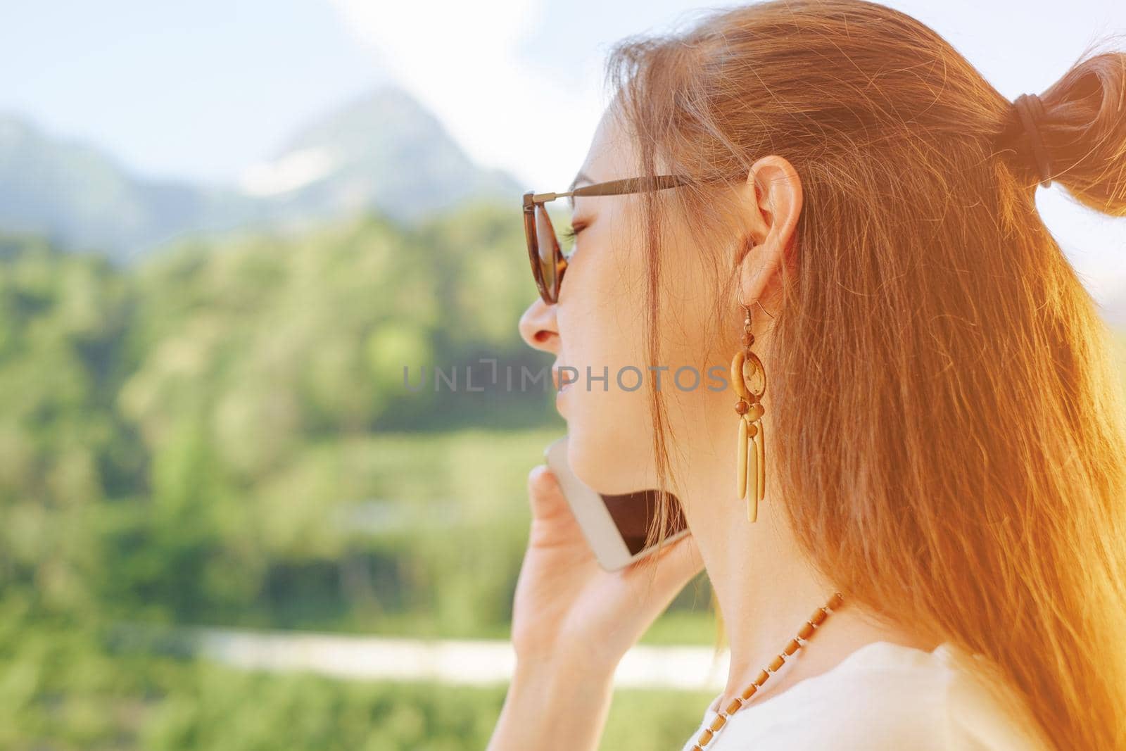 Portrait of young woman talking on phone on background of summer mountains.