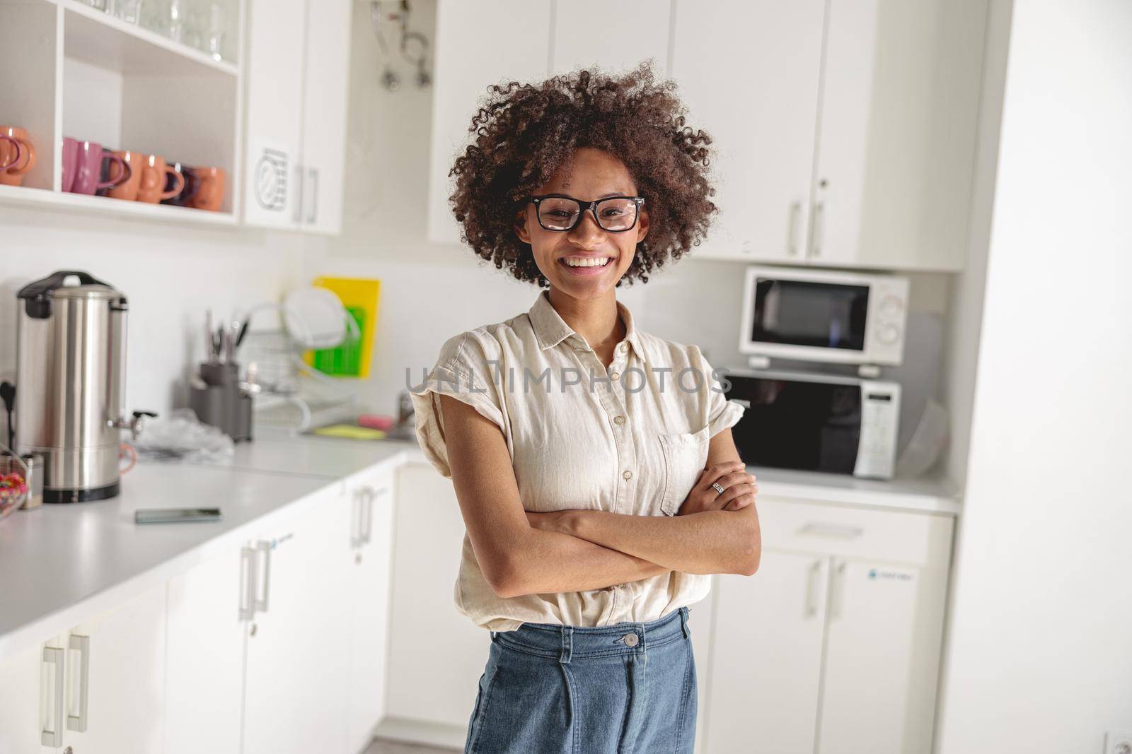 Happy Afro American woman with arms folded standing on office kitchen and looking at camera