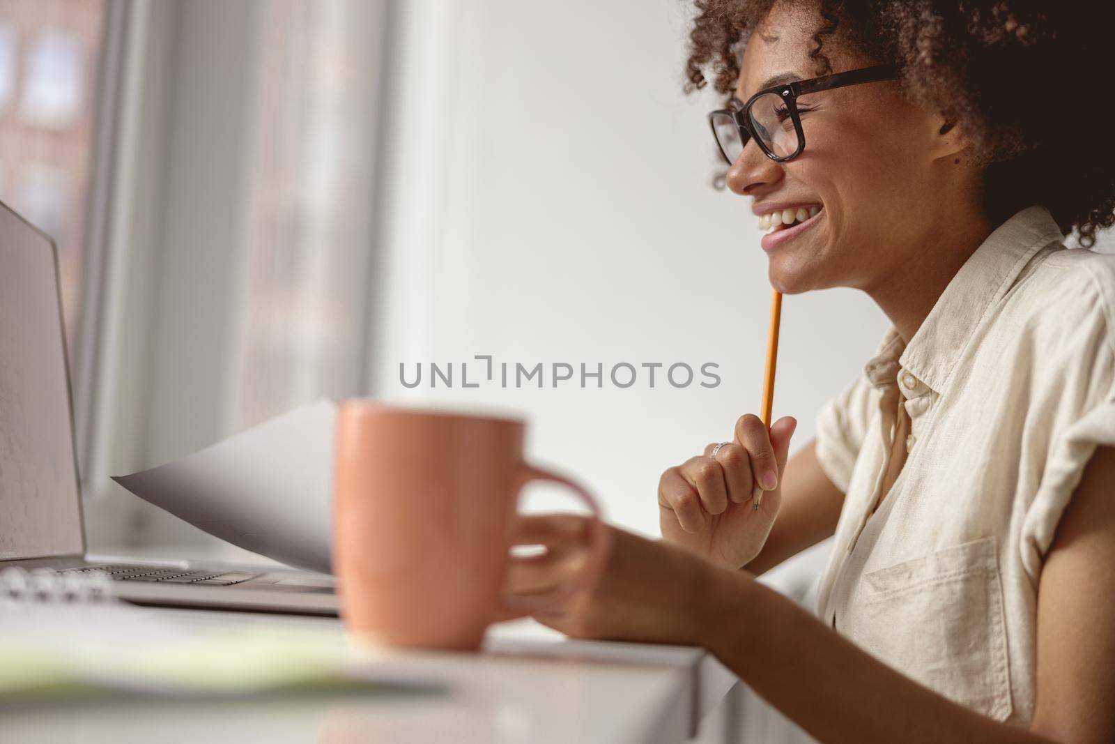 Smiling pretty woman holding document and pen while working with laptop in the office