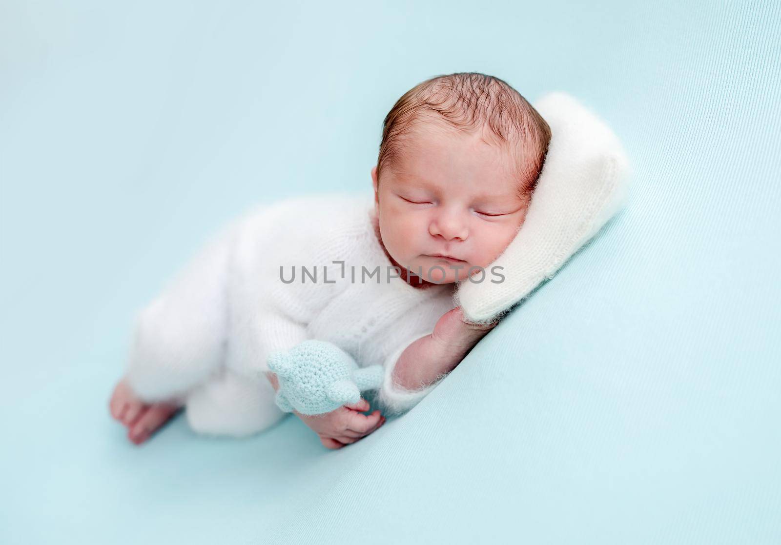 Lovely newborn in white clothes resting with head on tiny pillow