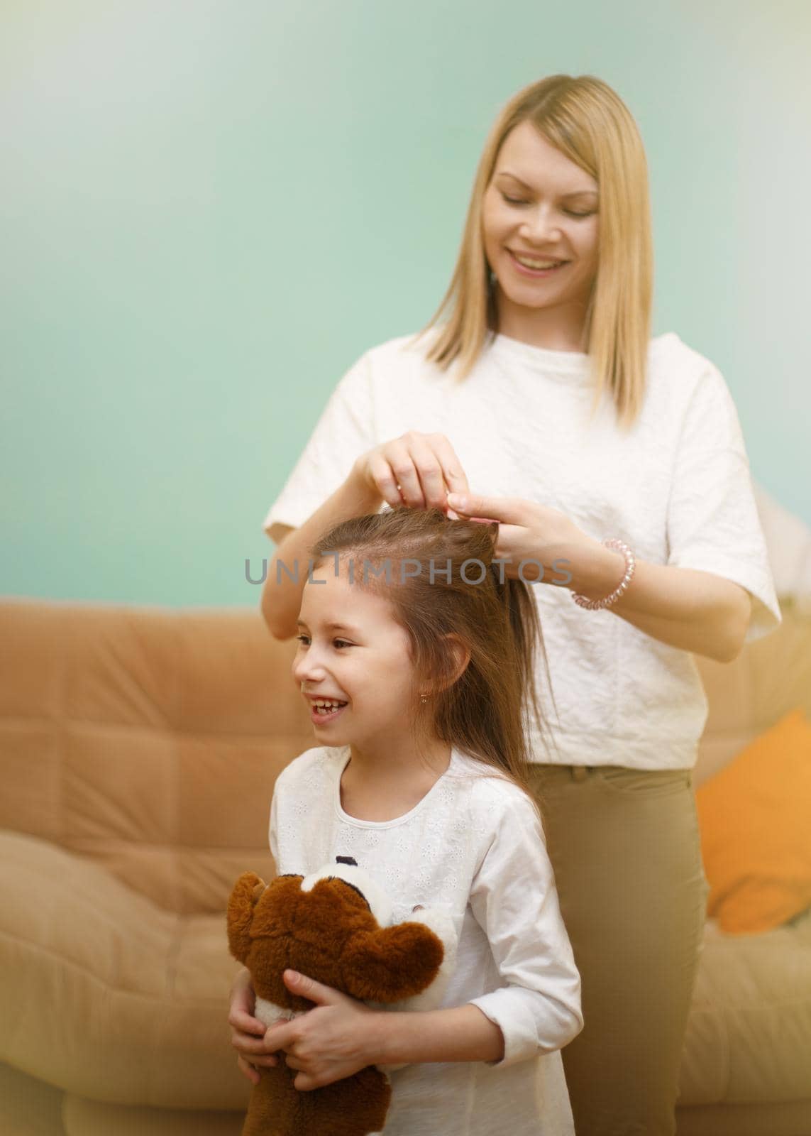 Mother is braiding her young daughter's hair standing in the children room. by alf061