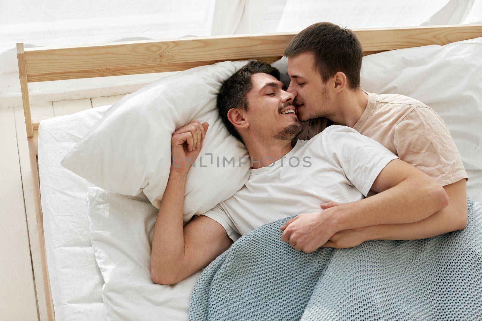 Happy gay couple lying on bed at home top view