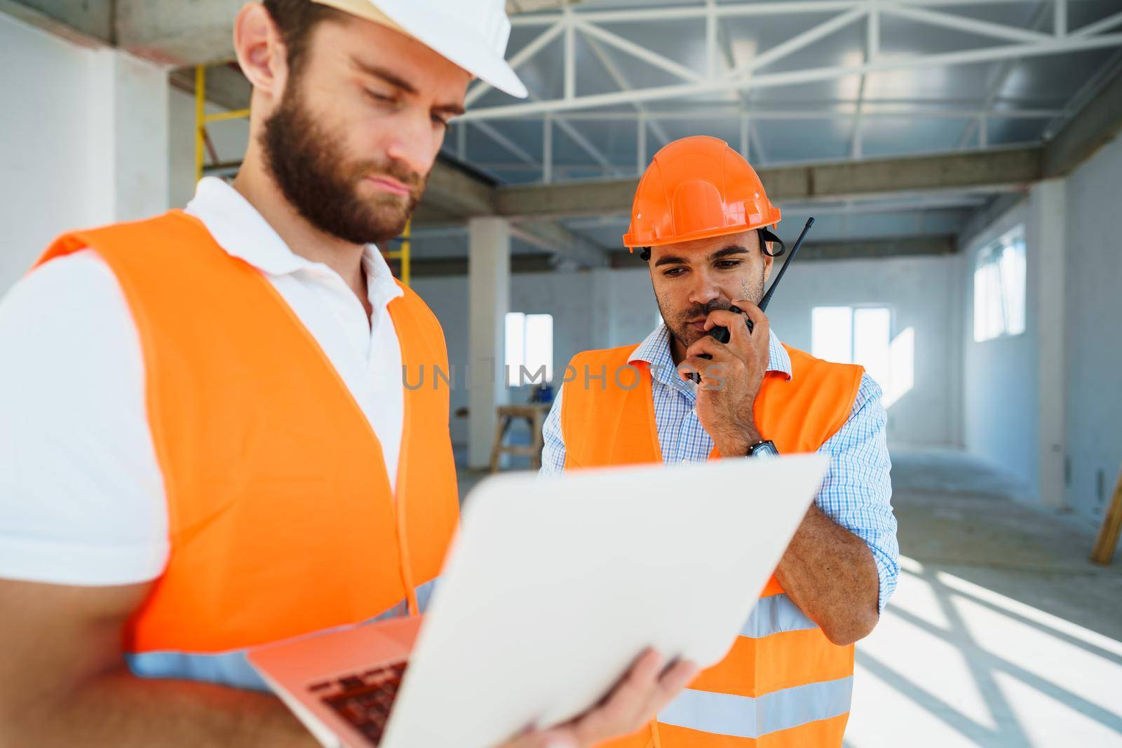 Two specialists supervisors in hardhats using laptop at construction site for work, close up