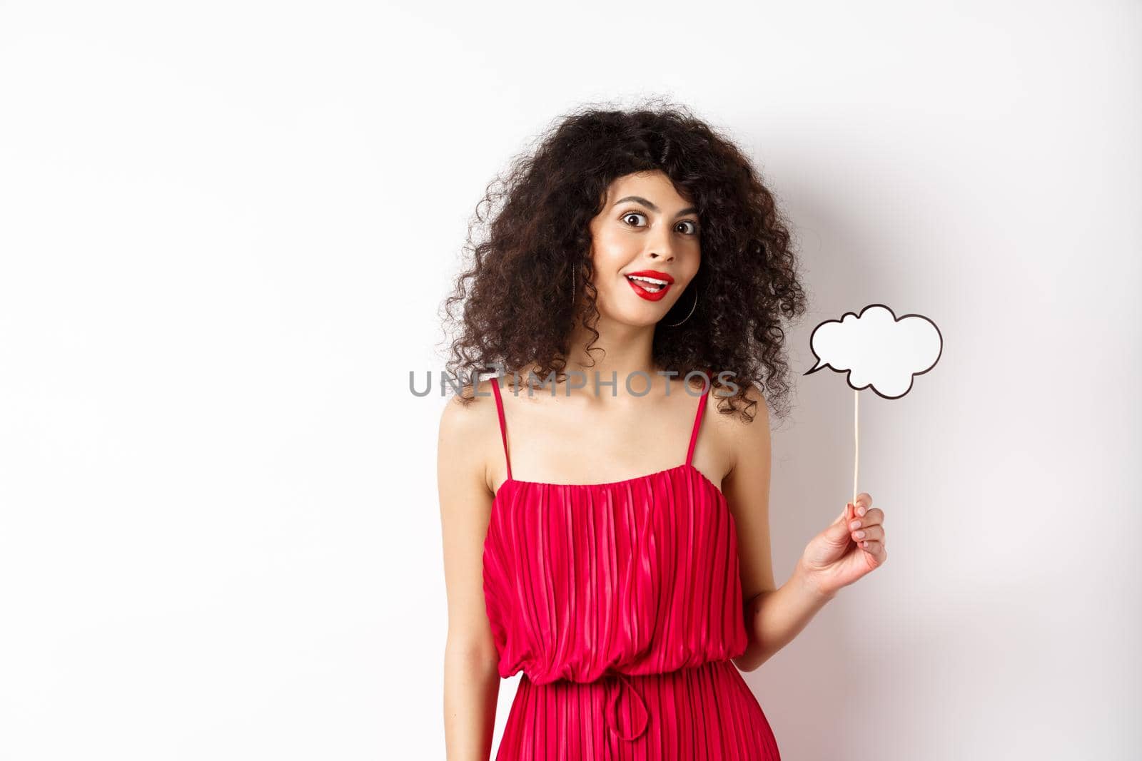Beautiful woman with curly hair, wearing red dress, holding comment cloud, say something, standing on white background.