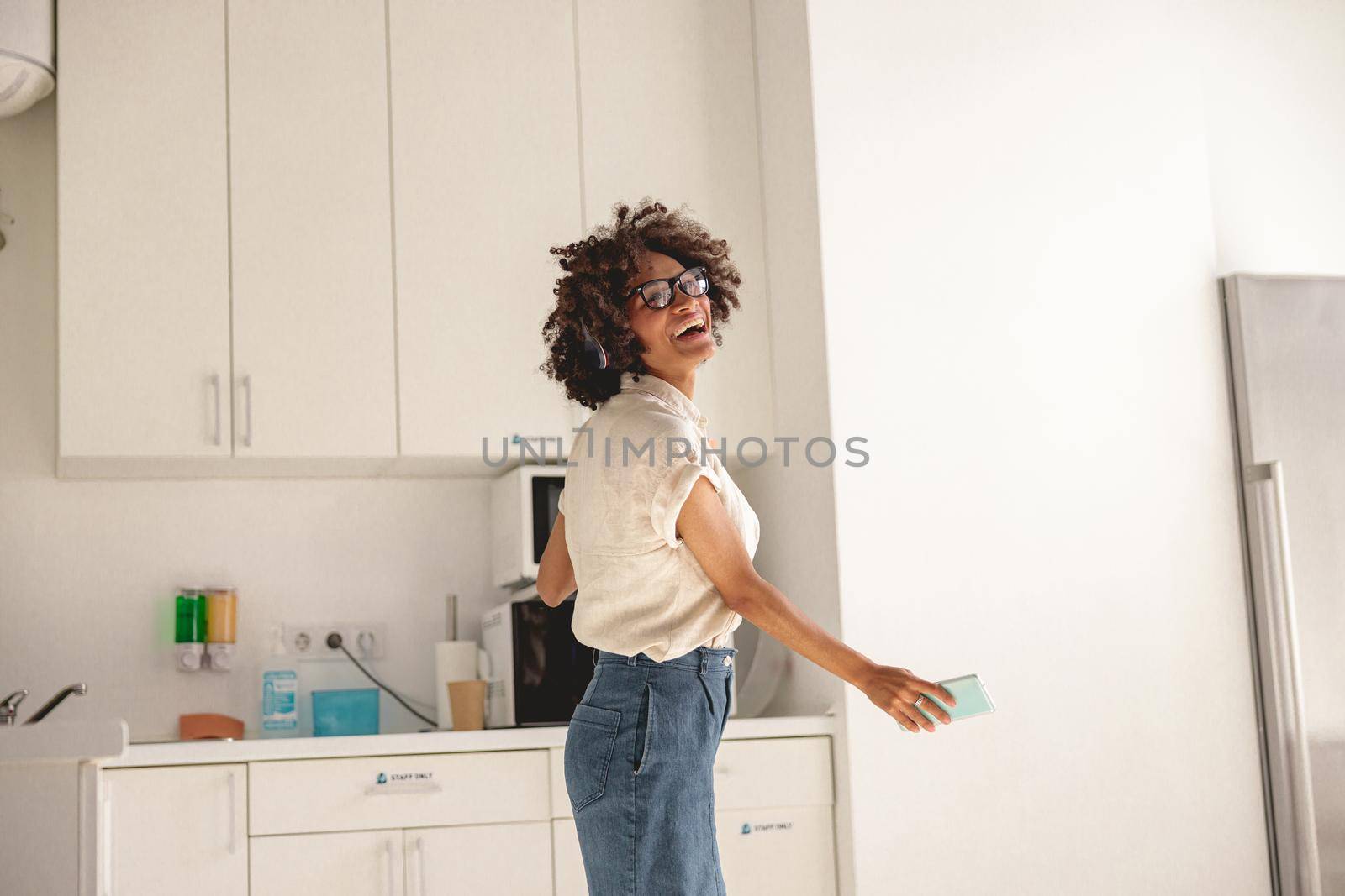 Happy Afro American woman holding mobile phone in hands while dancing by Yaroslav_astakhov