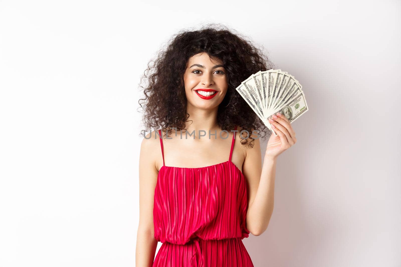 Stylish smiling woman in red dress showing money, standing on white background by Benzoix